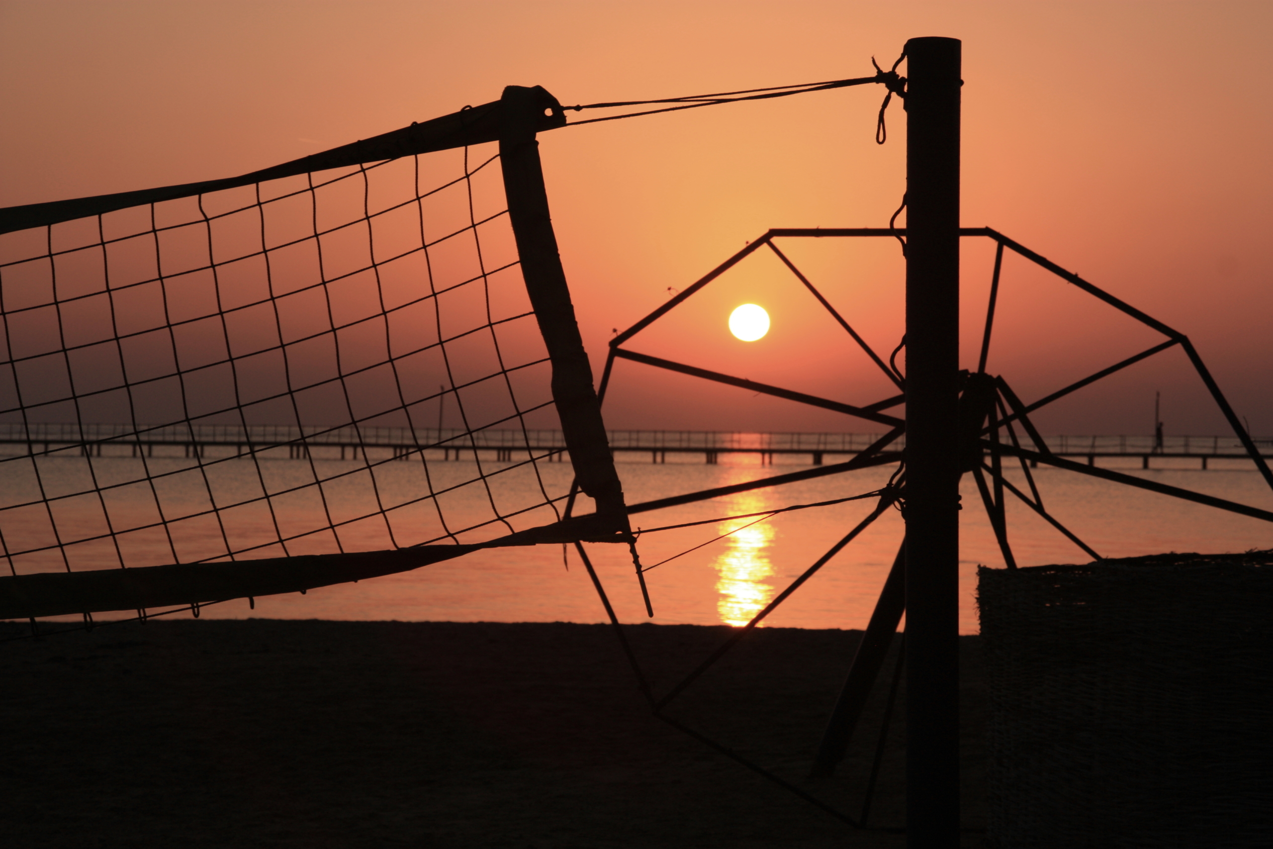 Sunrise with a silhouette of broken umbrella and volleyball net in EL Gouna